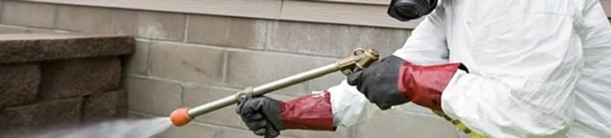 Pest control technician applying exterior insect treatment along a home foundation in Fresno, CA