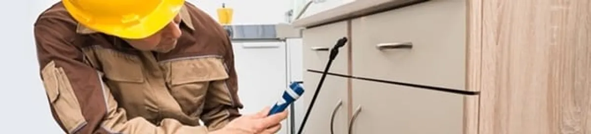 Roach exterminator applying treatment under kitchen cabinets in Fresno, CA