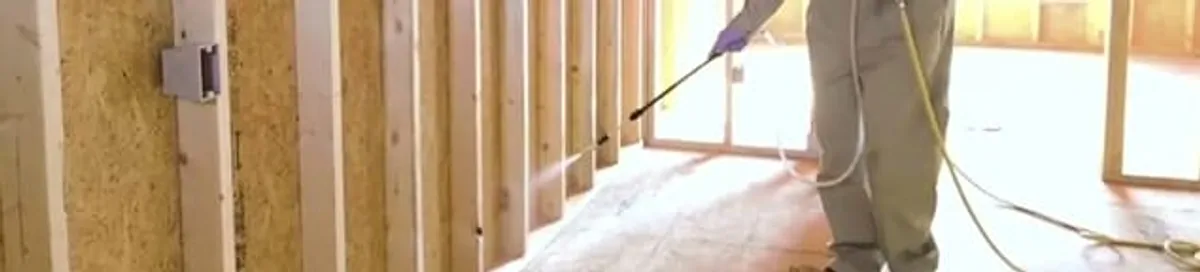 Termite treatment technician applying spray along framing and unfinished walls in Fresno, CA