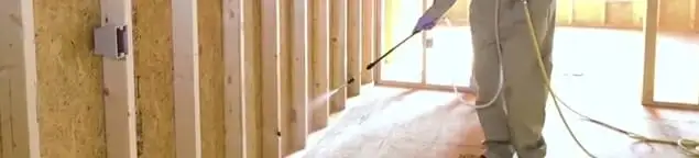 Termite treatment technician applying spray along framing and unfinished walls in Fresno, CA